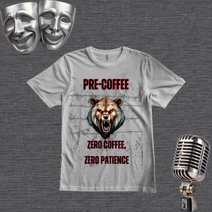 A gray graphic t-shirt featuring a roaring bear design with the text 'PRE COFFEE ZERO COFFEE, ZERO PATIENCE' in red and black. The t-shirt is displayed on a textured gray background alongside thematic props, including two silver comedy masks in the top-left and a vintage silver microphone in the bottom-right.