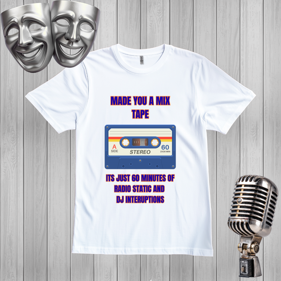 A white graphic t-shirt displayed on a gray wood plank background, flanked by silver comedy masks on the left and a vintage silver microphone on the right. The t-shirt features a retro cassette tape graphic with purple text reading 'MADE YOU A MIX TAPE' and 'ITS JUST 60 MINUTES OF RADIO STATIC AND DJ INTERUPTIONS'.