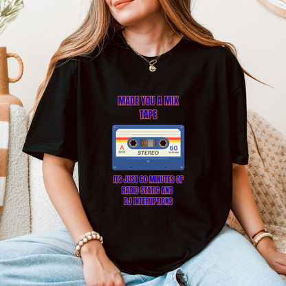 A woman wearing a black graphic t-shirt with a retro cassette tape design and the text 'MADE YOU A MIX TAPE' and 'ITS JUST 60 MINUTES OF RADIO STATIC AND DJ INTERRUPTIONS'.