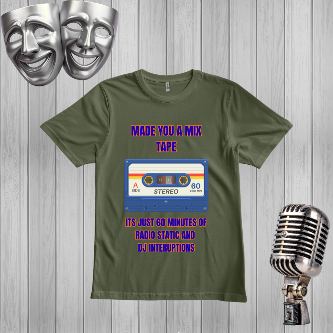 A green graphic t-shirt displayed on a light gray wood plank background, flanked by silver comedy masks on the left and a vintage silver microphone on the right. The t-shirt features a retro cassette tape graphic with the text 'MADE YOU A MIX TAPE' and 'ITS JUST 60 MINUTES OF RADIO STATIC AND DJ INTERRUPTIONS' in purple and orange.