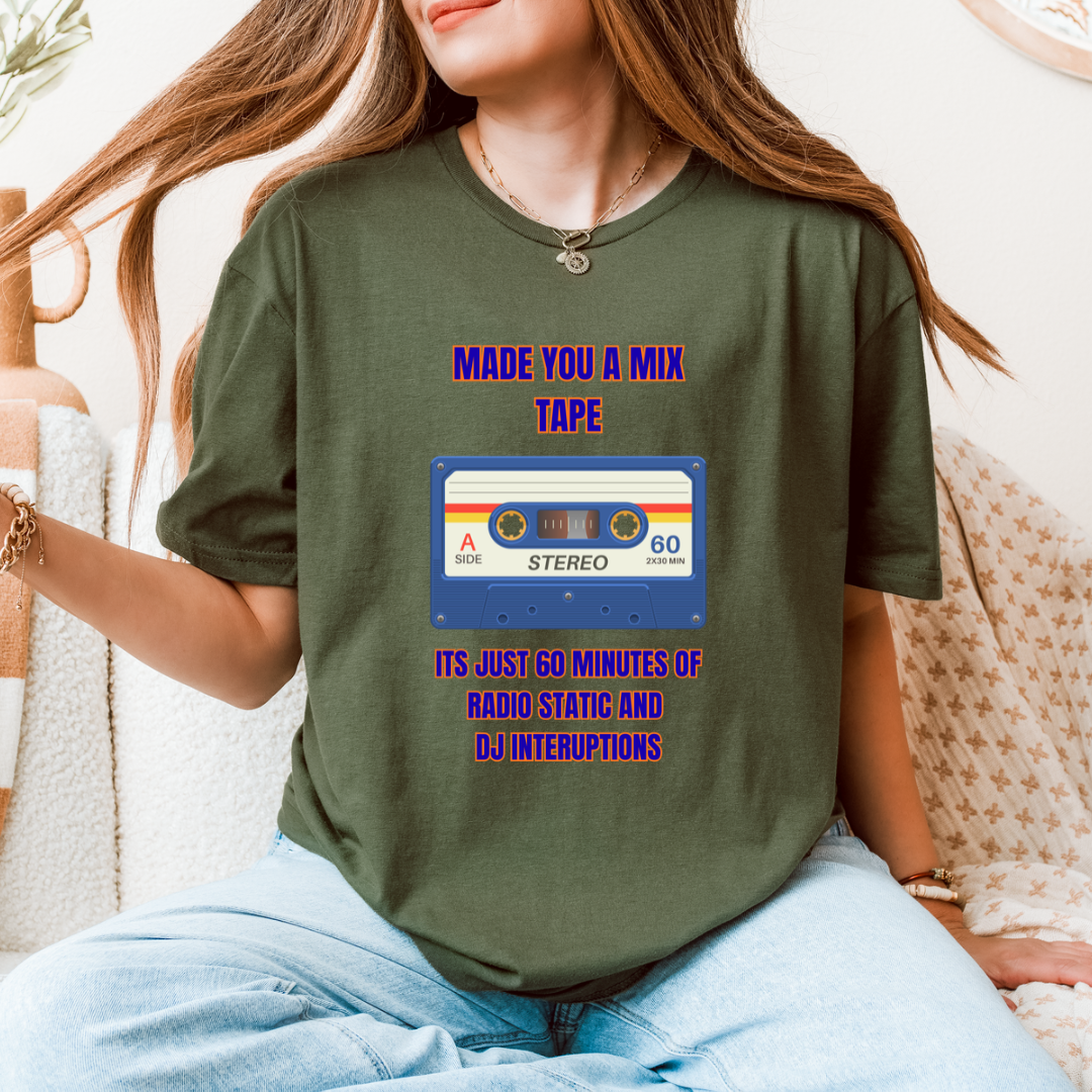 A woman wearing a green graphic t-shirt with a retro cassette tape design and purple text that reads 'MADE YOU A MIX TAPE ITS JUST 60 MINUTES OF RADIO STATIC AND DJ INTERRUPTIONS'.