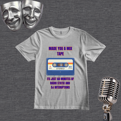 A gray graphic t-shirt displayed flat on a dark gray textured background, flanked by two silver comedy masks at the top and a vintage silver microphone at the bottom right. The t-shirt features a retro cassette tape graphic with the text 'MADE YOU A MIX TAPE' in purple and blue, and 'ITS JUST 60 MINUTES OF RADIO STATIC AND DJ INTERUPTIONS' in blue and purple.