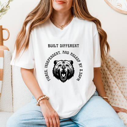 A woman wearing a white graphic t-shirt with a black bear design and the text 'BUILT DIFFERENT FIERCE, INDEPENDENT, AND ASLEEP BY & SLEEP BY' 8.30PM.
