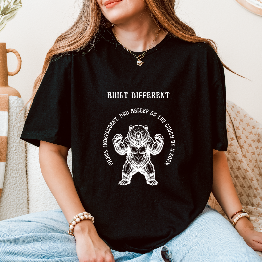 A woman wearing a black graphic t-shirt with a white bear design and the text 'BUILT DIFFERENT' 