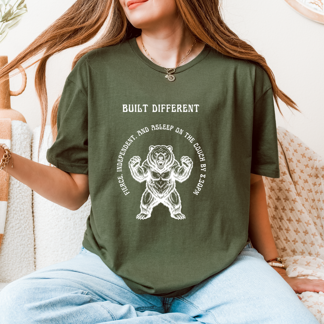 A woman wearing a green graphic t-shirt with a white bear design and the text 'BUILT DIFFERENT' 