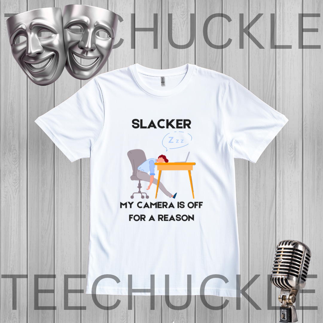 A white graphic t-shirt displayed on a gray wood plank background, featuring a cartoon illustration of a person sleeping at a desk with the text 'SLACKER, MY CAMERA IS OFF FOR A REASON'. The image includes decorative props like silver theater masks and a vintage microphone, 