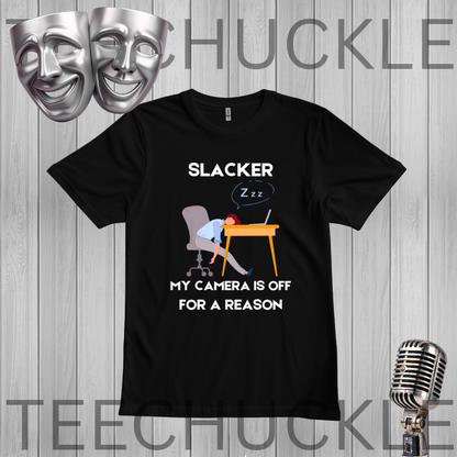 A black graphic t-shirt displayed on a gray wood plank background, featuring a cartoon illustration of a person sleeping at a desk with the text 'SLACKER, MY CAMERA IS OFF FOR A REASON'. The image includes decorative props like silver theater masks and a vintage microphone, 