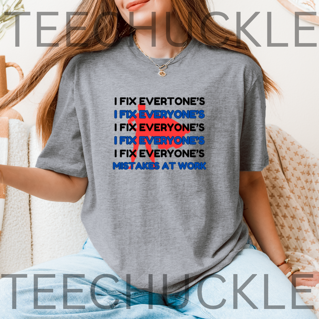 A Grey graphic t-shirt, featuring a text design that reads 'I FIX EVERYONE'S MISTAKES AT WORK' with a red scribble over repeated 'I FIX EVERYONE'S' lines. 