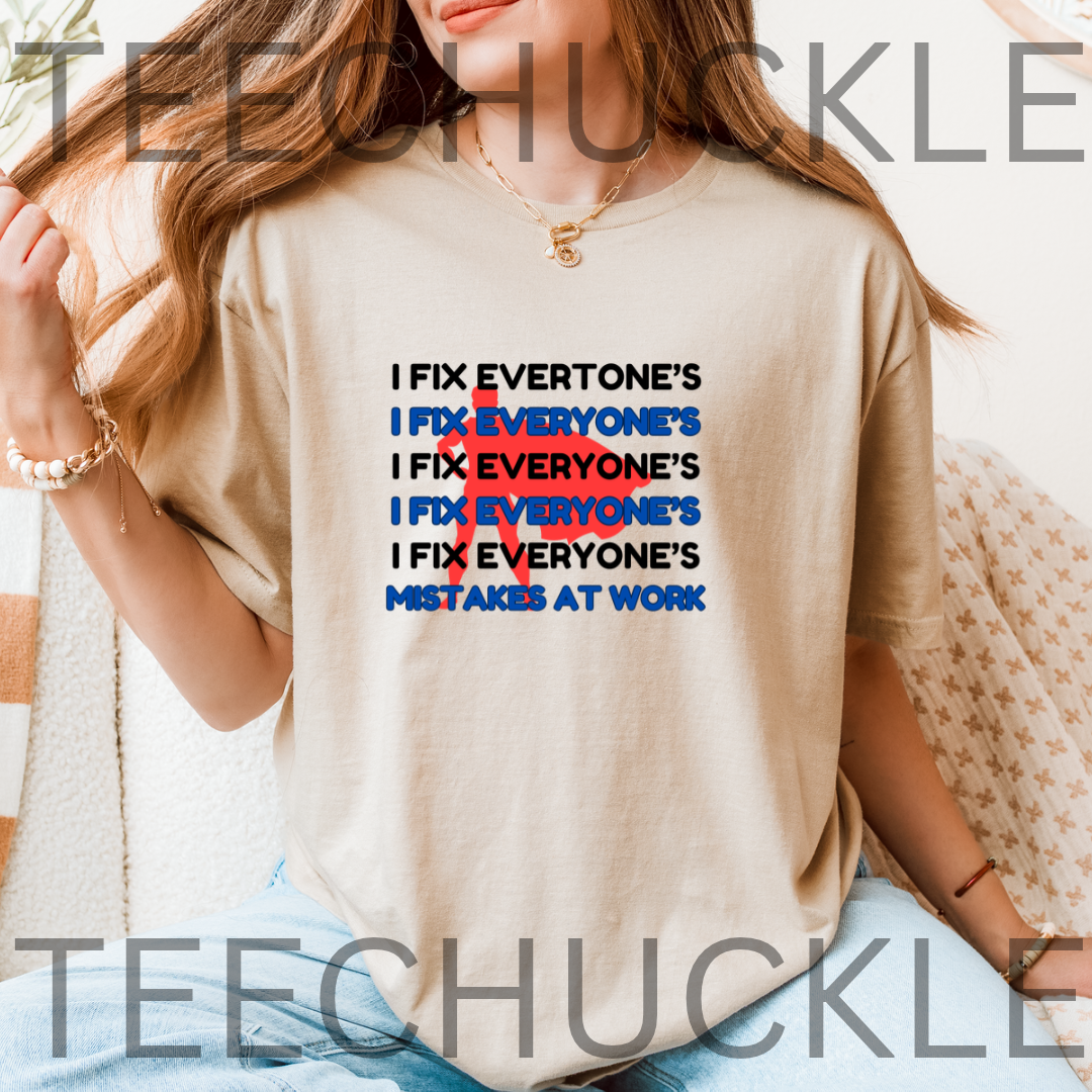 A woman wearing a sand graphic t-shirt with the slogan 'I FIX EVERYONE'S MISTAKES AT WORK' repeated in black and blue, crossed out in red. 