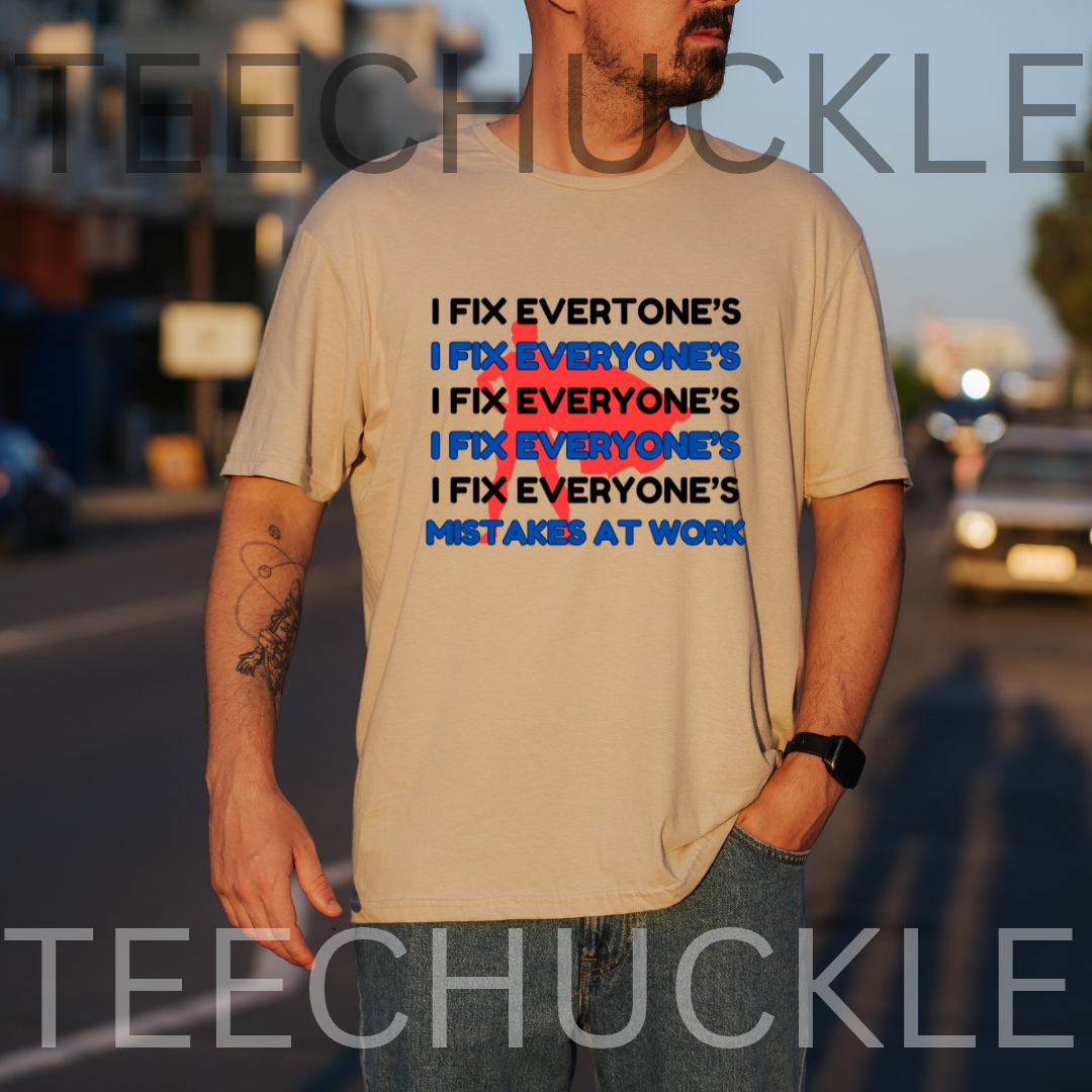 A man wearing a sand graphic t-shirt with the slogan 'I FIX EVERYONE'S MISTAKES AT WORK' repeated in black and blue text, set against a blurred street background at sunset.
