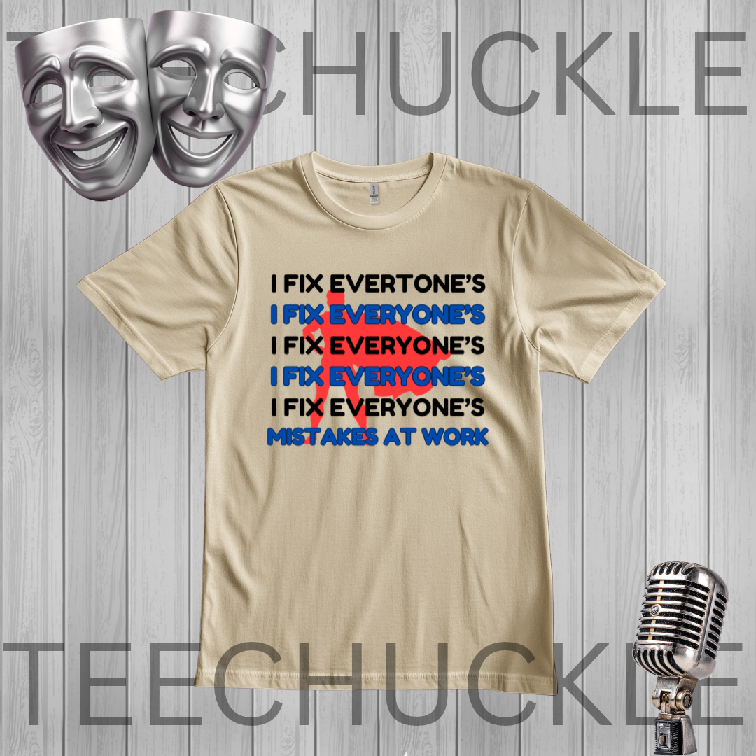 A sand graphic t-shirt displayed on a gray wood-plank background, featuring a humorous text design about fixing mistakes at work in black, red, and blue. The image includes decorative silver theater masks in the top left and a vintage microphone in the bottom right,