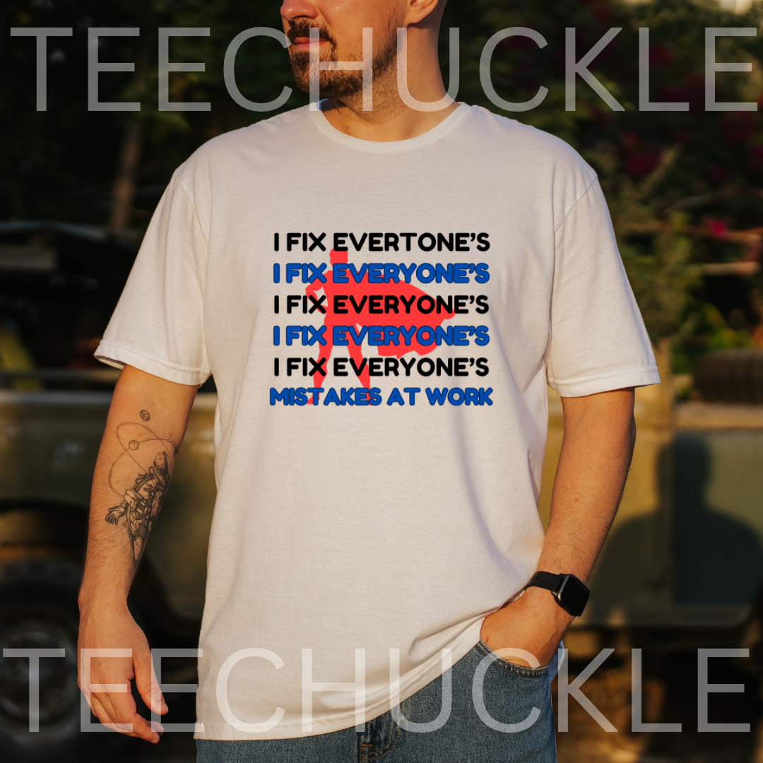 A man wearing a white graphic t-shirt with the slogan 'I FIX EVERYONE'S MISTAKES AT WORK' repeated in black and blue, with a red cross graphic. 