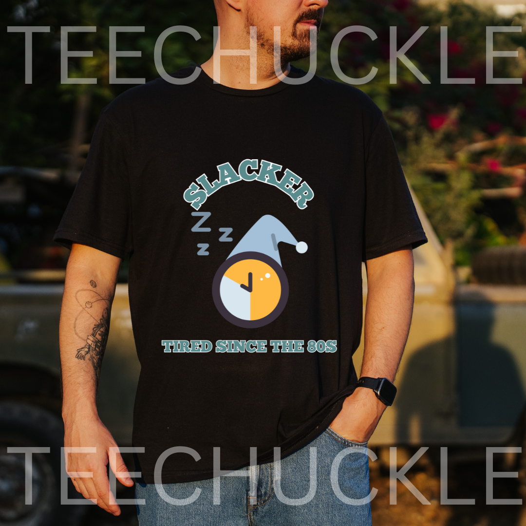 A man wearing a black graphic t-shirt with a 'Slacker' sleeping clock design, set against an outdoor blurred background 