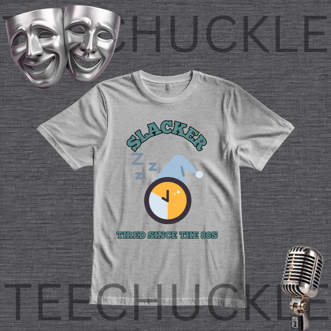 A gray graphic t-shirt featuring a 'Slacker' theme with a sleeping clock and the text 'Tired Since the 80s'. The t-shirt is displayed on a dark gray textured background with theatrical comedy masks, a vintage microphone