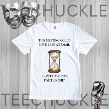 A white graphic t-shirt displayed on a gray wood-plank background, featuring a humorous meeting procrastination quote and an hourglass illustration. The image includes decorative props like silver theater masks and a vintage microphone
