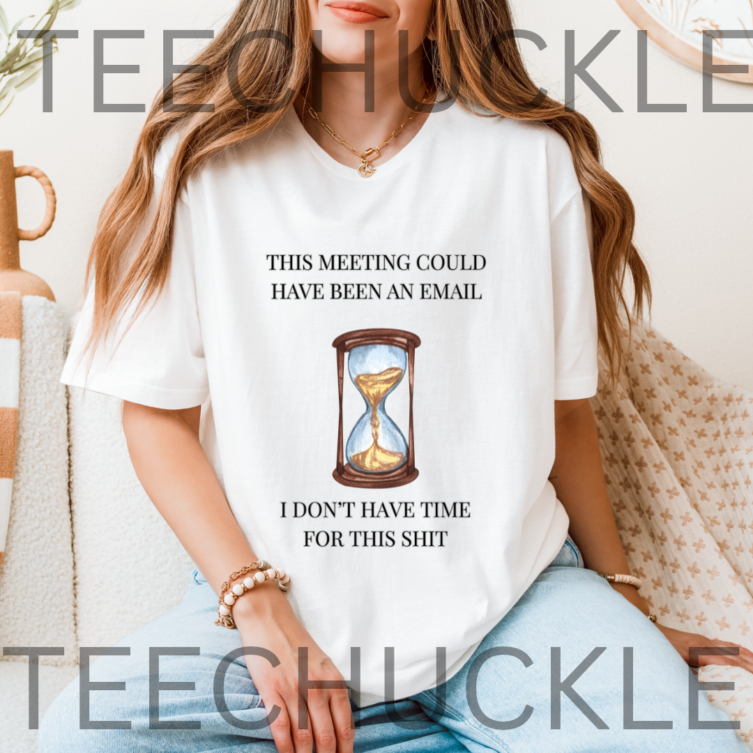 A woman wearing a white graphic t-shirt with a humorous email meeting message and an hourglass illustration. The t-shirt features the text 'THIS MEETING COULD HAVE BEEN AN EMAIL' above the graphic and 'I DON'T HAVE TIME FOR THIS SHIT' below.