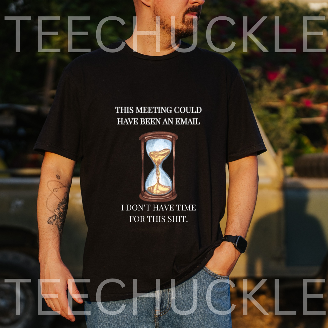 A man wearing a black graphic t-shirt with a humorous meeting-related slogan and an hourglass illustration, set against an outdoor blurred background. 