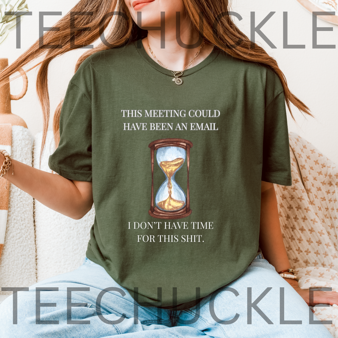 A woman wearing a green graphic t-shirt with a humorous text print and an hourglass illustration. The t-shirt features the text 'THIS MEETING COULD HAVE BEEN AN EMAIL' above the graphic and 'I DON'T HAVE TIME FOR THIS SHIT.