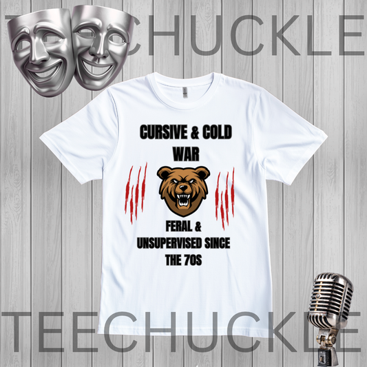 A white graphic t-shirt displayed on a gray wood plank background, featuring a bear head illustration, red claw marks, and the text 'CURSIVE & COLD WAR FERAL & UNSUPERVISED SINCE THE 70S'. The image includes decorative silver theater masks in the top left and a vintage microphone in the bottom right