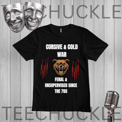A black short-sleeve graphic t-shirt displayed on a gray wood-plank background. The shirt features a design with the text 'CURSIVE & COLD WAR' and 'FERAL & UNSUPERVISED SINCE THE 70S' in white, flanking a brown bear head graphic and red claw marks.