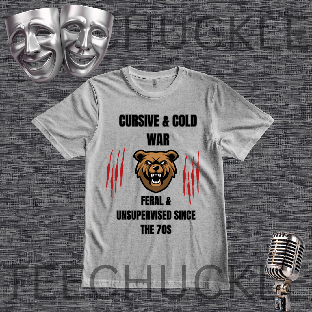 A gray graphic t-shirt displayed on a dark gray textured background, featuring a bear graphic and the text 'CURSIVE & COLD WAR FERAL & UNSUPERVISED SINCE THE 70S'. The image includes decorative props like silver theater masks, a vintage microphone