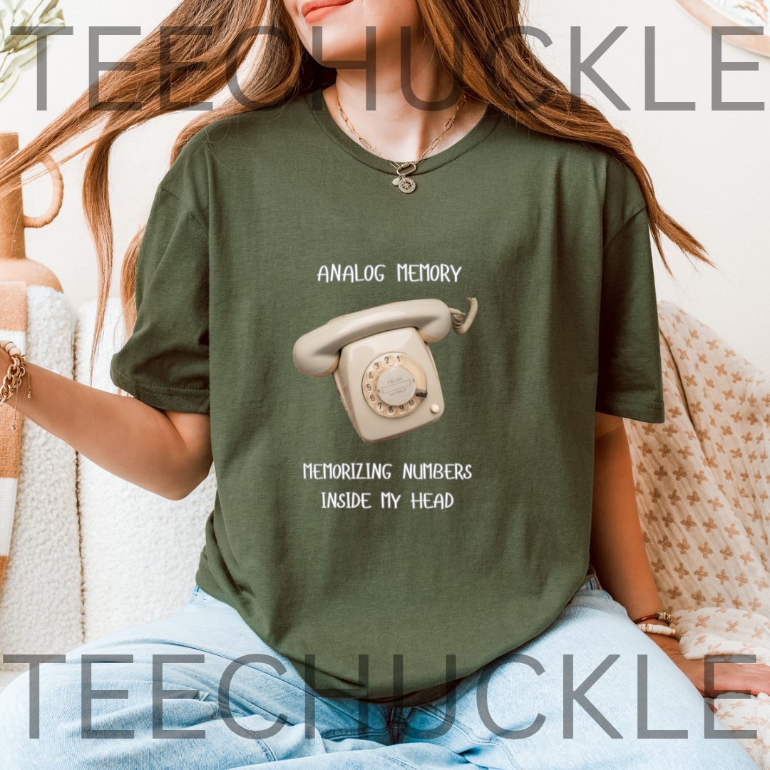 A woman wearing a green graphic t-shirt with a retro rotary phone design and the text 'ANALOGIC MEMORY MEMORIZING NUMBERS INSIDE MY HEAD'. 
