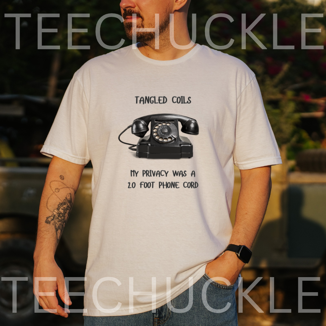 A man wearing a white graphic t-shirt with a black rotary phone print and the text 'Tangled Coils' and 'My Privacy Was a 2 Foot Phone Cord', and is taken in an outdoor setting.