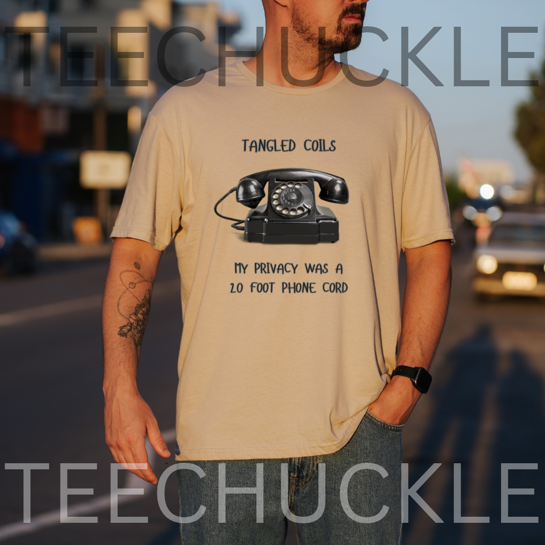 A man wearing a sand graphic t-shirt with a black rotary phone print and the text 'Tangled Coils My Privacy Was A 2.0 Foot Phone Cord'.