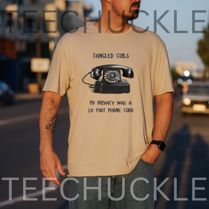A man wearing a sand graphic t-shirt with a black rotary phone print and the text 'Tangled Coils My Privacy Was A 2.0 Foot Phone Cord'.