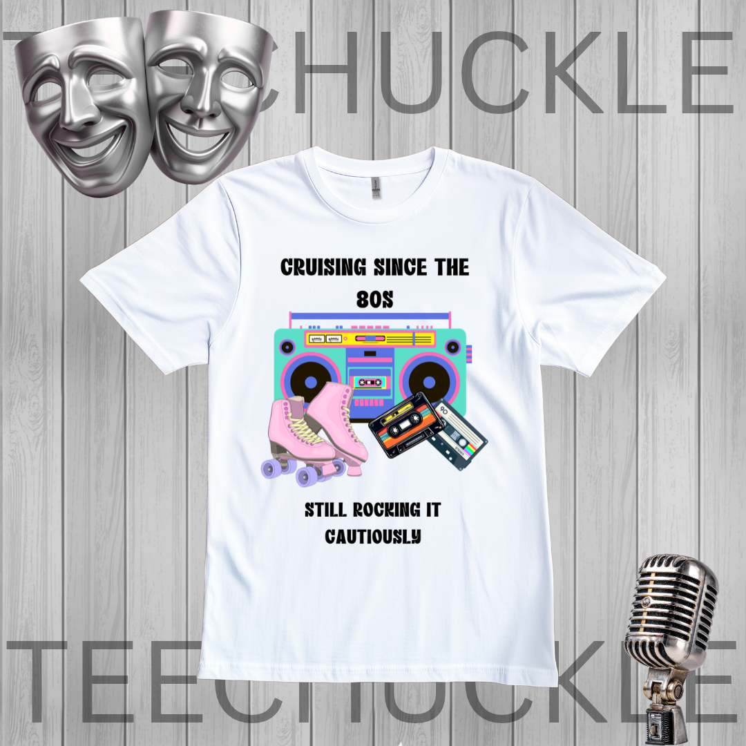A white graphic t-shirt displayed on a gray wood plank background, featuring a retro 80s design with a boombox, pink roller skate, cassette tapes, and the text 'CRUISING SINCE THE 80S STILL ROCKING IT CAUTIOUSLY'. The image includes decorative silver theater masks and a vintage microphone