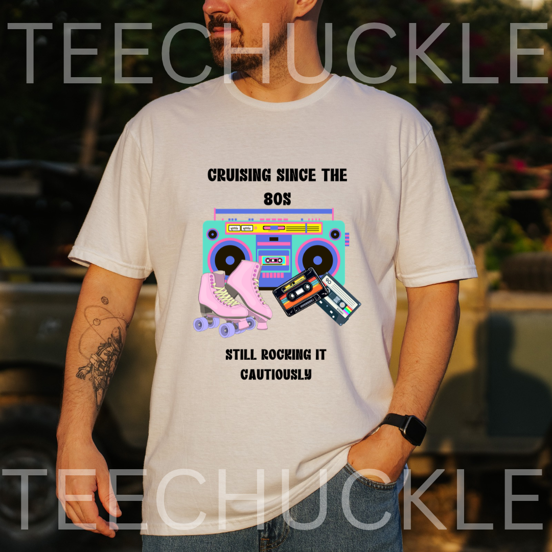 A man wearing a white graphic t-shirt with a retro 80s boombox and roller skate design, set against an outdoor blurred background. The shirt features the text 'CRUISING SINCE THE 80S' and 'STILL ROCKING IT CAUTIOUSLY'.