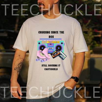 A man wearing a white graphic t-shirt with a retro 80s boombox and roller skate design, set against an outdoor blurred background. The shirt features the text 'CRUISING SINCE THE 80S' and 'STILL ROCKING IT CAUTIOUSLY'.