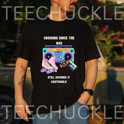 A man wearing a black graphic t-shirt with a retro 80s boombox, roller skates, and cassette tapes design, featuring the text 'CRUISING SINCE THE 80S STILL ROCKING IT CAUTIOUSLY'.
