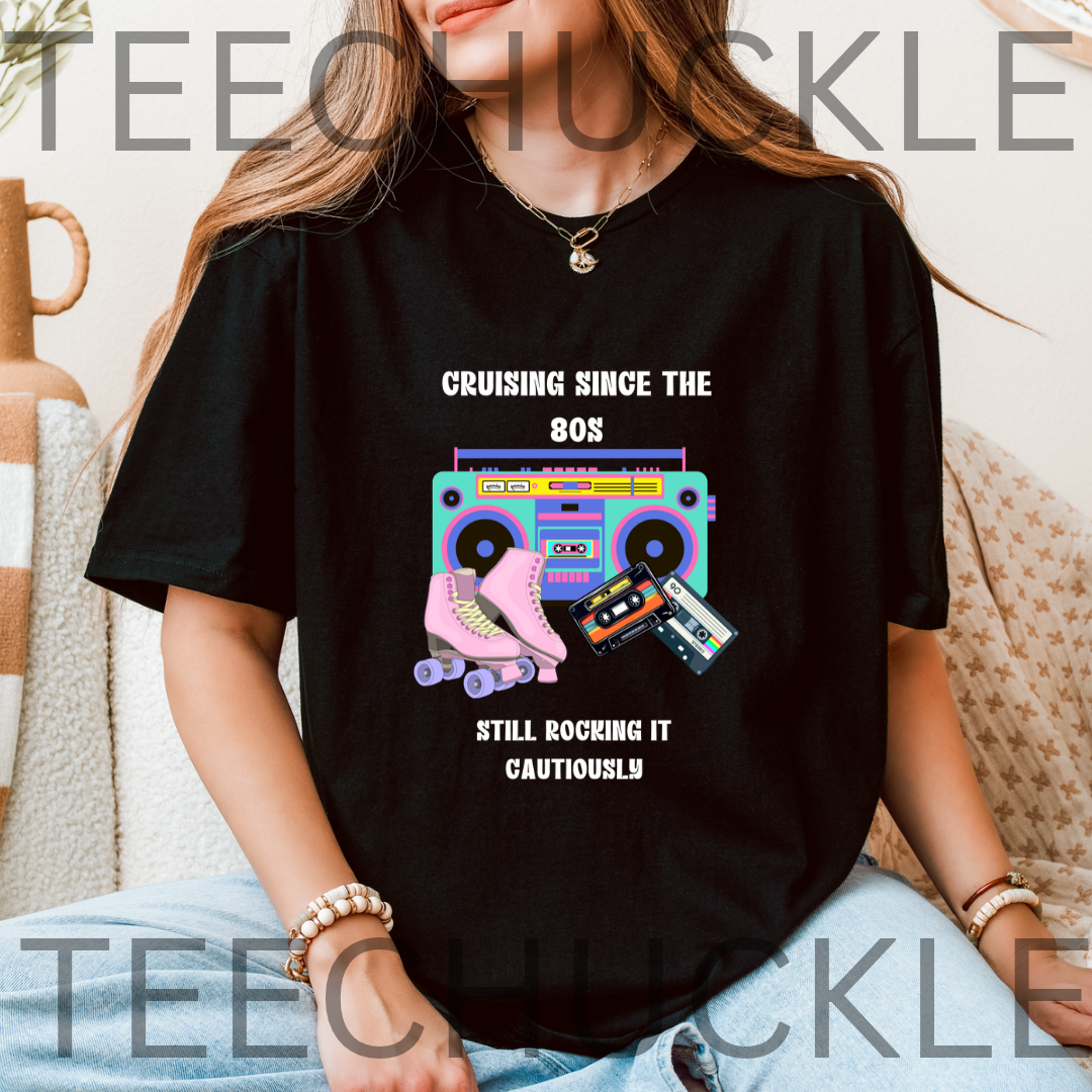 A woman wearing a black graphic t-shirt with a retro 80s theme. The shirt features a colorful boombox, cassette tapes, roller skates, and the text 'CRUISING SINCE THE 80S STILL ROCKING IT CAUTIOUSLY'.