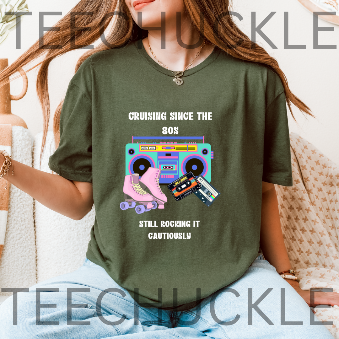 A woman wearing a green graphic t-shirt with a retro 80s theme, featuring a pink roller skate, cassette tapes, and a boombox with the text 'Cruising since the 80s Still rocking it cautiously'.
