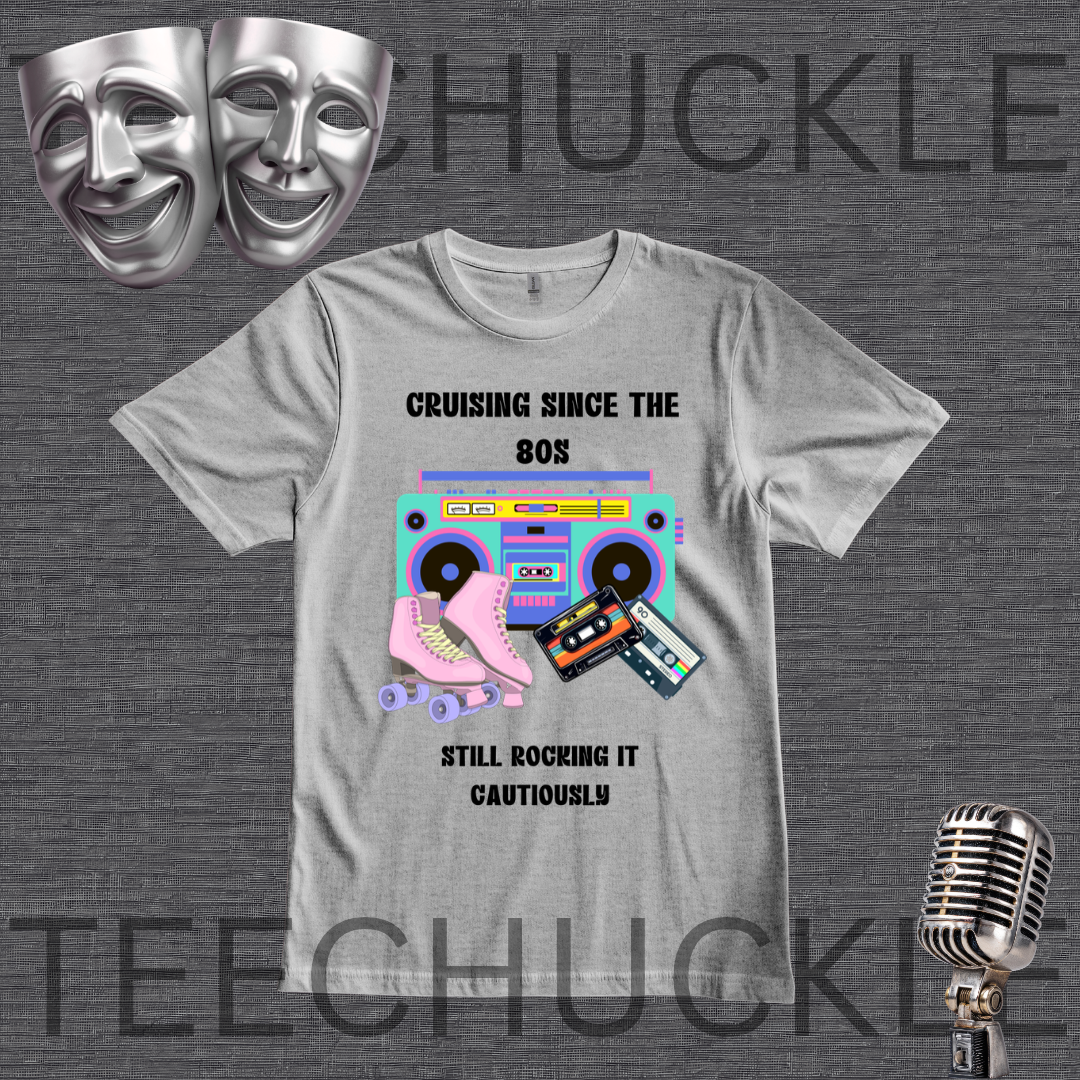 A light gray graphic t-shirt featuring a retro 80s theme with a boombox, roller skate, and cassette tapes, accompanied by the text 'CRUISING SINCE THE 80S STILL ROCKING IT CAUTIONLY'. The t-shirt is displayed on a dark gray textured background with silver theater masks, a vintage microphone
