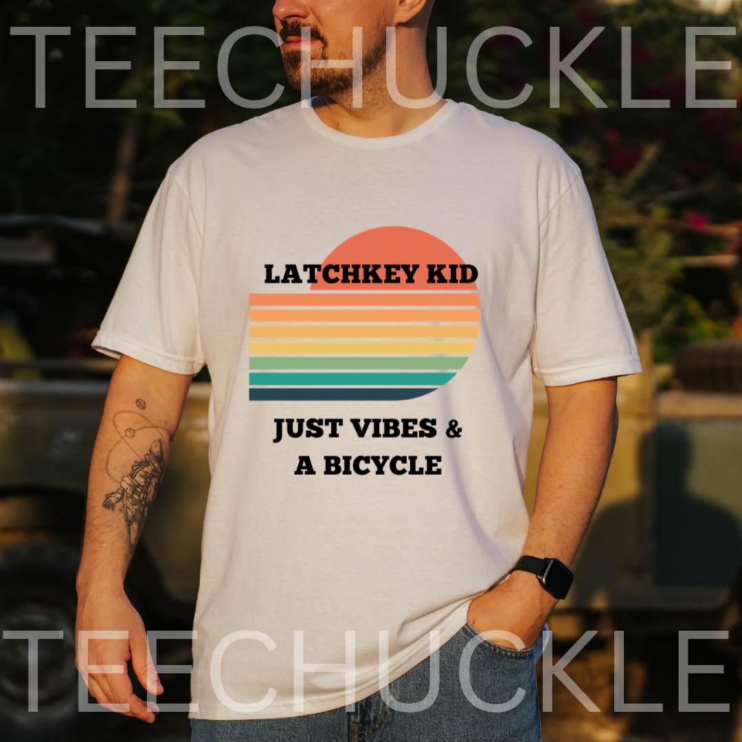 A man wearing a white graphic t-shirt with a retro sunset design and the text 'LATCHKEY KID JUST VIBES & A BICYCLE'. The background is a blurred outdoor setting