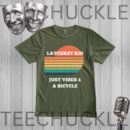 A green graphic t-shirt displayed on a gray wood-plank background. The shirt features a retro sunset design with horizontal stripes in orange, yellow, and teal, with the text 'LATCHKEY KID' and 'JUST VIBES & A BICYCLE' in white.