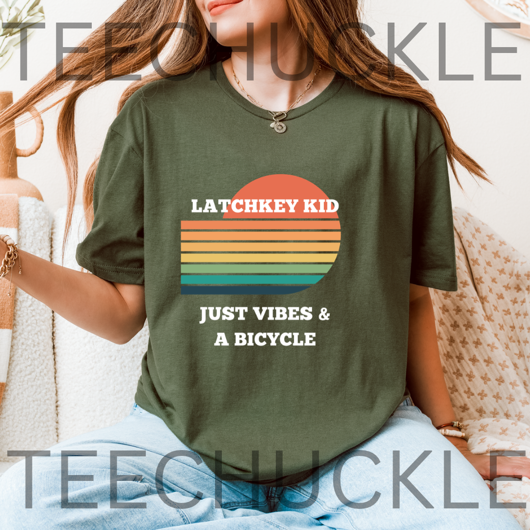 A woman wearing a green graphic t-shirt with a retro sunset design and the text 'LATCHKEY KID JUST VIBES & A BICYCLE'.