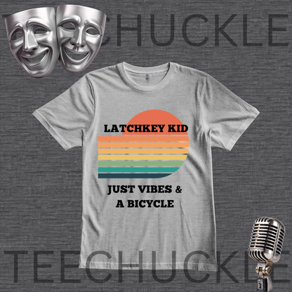 A gray graphic t-shirt displayed on a dark gray textured background. The shirt features a retro sunset graphic with orange, yellow, and green stripes, and the text 'LATCHKEY KID JUST VIBES & A BICYCLE'.