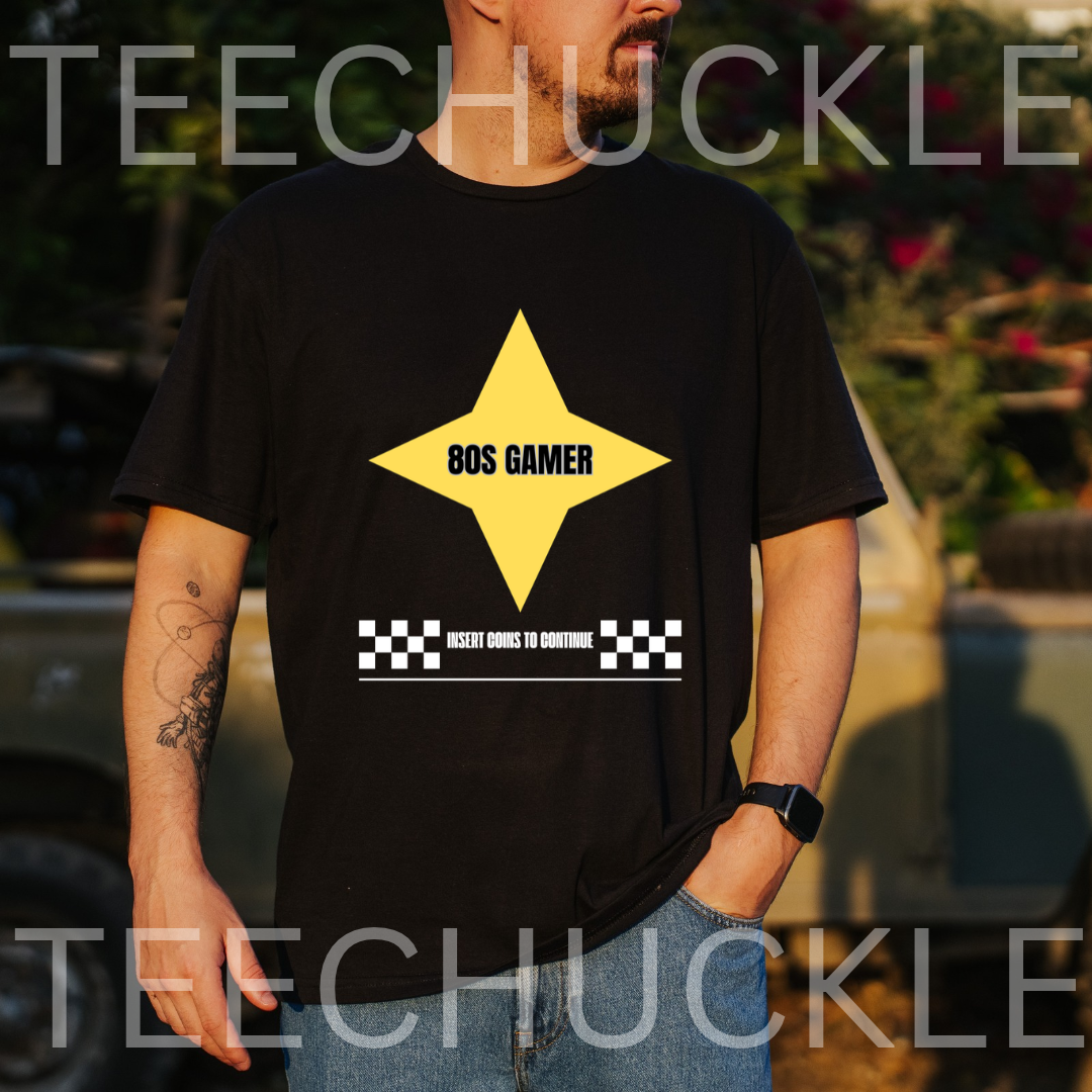 A man wearing a black graphic t-shirt with a yellow star and '80S GAMER' text, set against a blurred outdoor background. 