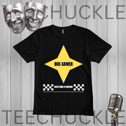 A black short-sleeve graphic t-shirt displayed flat against a gray wood-plank background. The shirt features a large yellow star graphic with the text '80S GAMER' in black, and a white text bar below reading 'INSERT COINS TO CONTINUE' flanked by black-and-white checkered squares.