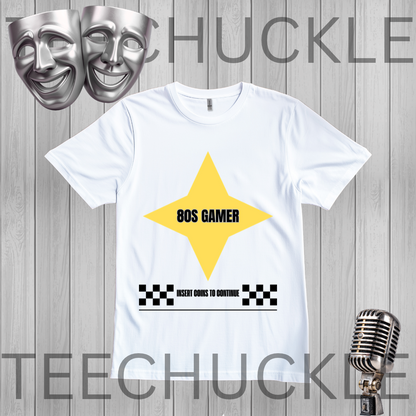 A white short-sleeve t-shirt with a yellow star graphic and '80S GAMER' text, displayed on a gray wood-plank background with theatrical masks, a vintage microphone