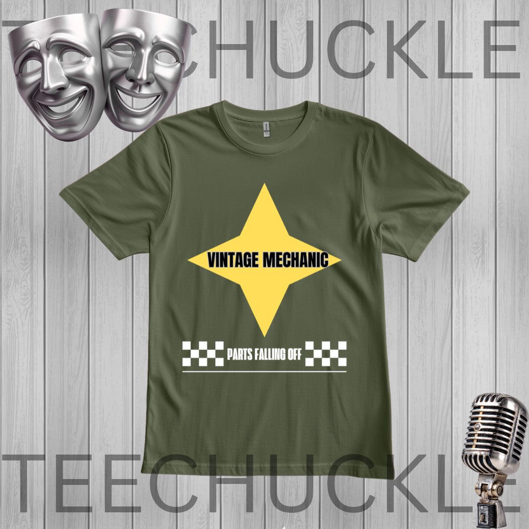 A green graphic t-shirt featuring a yellow star with 'VINTAGE MECHANIC' in black text and a white checkered bar below reading 'PARTS FALLING OFF'. The t-shirt is displayed on a gray wood-plank background  flanked by silver comedy and tragedy masks on the top left and a vintage microphone on the bottom right.