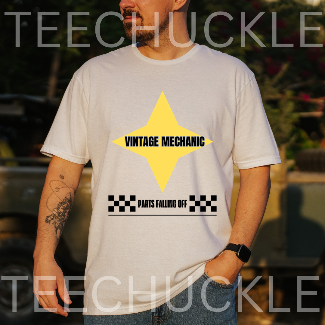 A man wearing a white graphic t-shirt with a yellow star and black text reading 'VINTAGE MECHANIC' and 'PARTS FALLING OFF'. The background is a blurred outdoor setting with a vintage car, 
