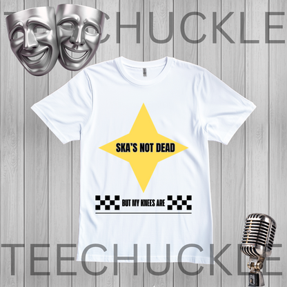 A white short-sleeve graphic T-shirt. The shirt has a large yellow star shape with the text 'SKA'S NOT DEAD' in black, plus a black-and-white checkered bar and the phrase 'BUT MY KNEES ARE' below.