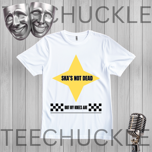 A white short-sleeve graphic T-shirt. The shirt has a large yellow star shape with the text 'SKA'S NOT DEAD' in black, plus a black-and-white checkered bar and the phrase 'BUT MY KNEES ARE' below.
