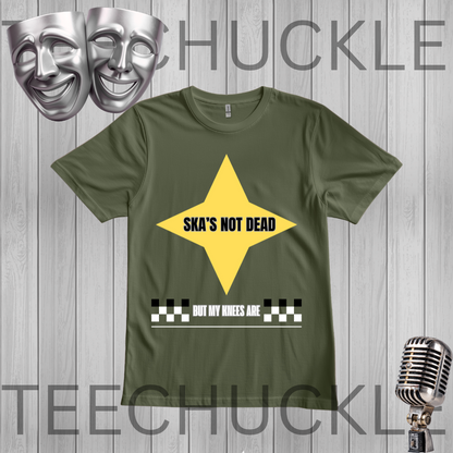 A green graphic t-shirt displayed on a gray wood-plank background. The shirt features a yellow diamond graphic with the text 'SKA'S NOT DEAD' in black, and a white text banner below reading 'BUT MY KNEES ARE' with a black and white checkered bar.