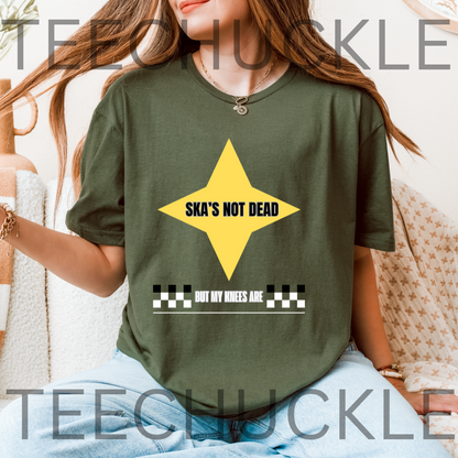 A woman wearing an oversized green graphic t-shirt with a yellow star and the text 'SKA'S NOT DEAD BUT MY KNEES ARE'. 