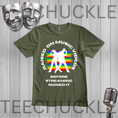 A green graphic t-shirt displayed on a gray wood-plank background. The shirt features a white circular text graphic reading 'RAISED ON MUSIC VIDEOS BEFORE STREAMING RUINED IT' surrounding a white silhouette of a person dancing in front of a retro rainbow-striped background.